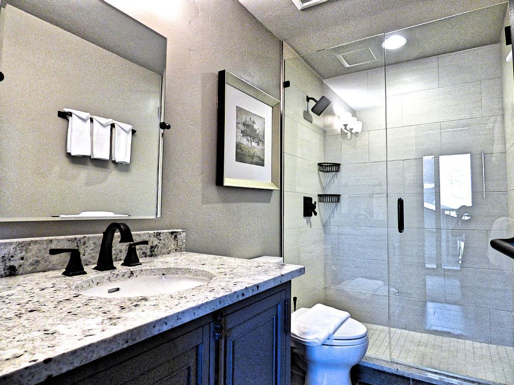 Une salle de bain moderne avec un lavabo surmonté d’un plan de travail en granit, un grand miroir et une douche séparée par des parois en verre.