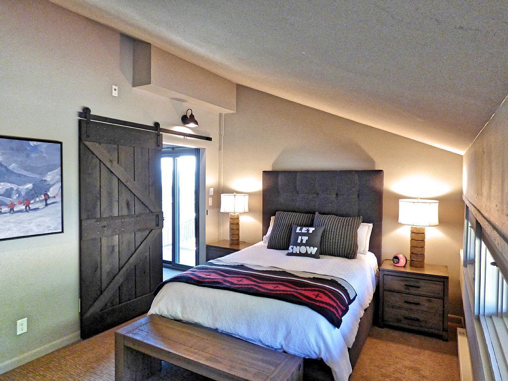 Une chambre à coucher avec un grand lit, un banc, une porte coulissante de style grange et deux lampes de chevet.