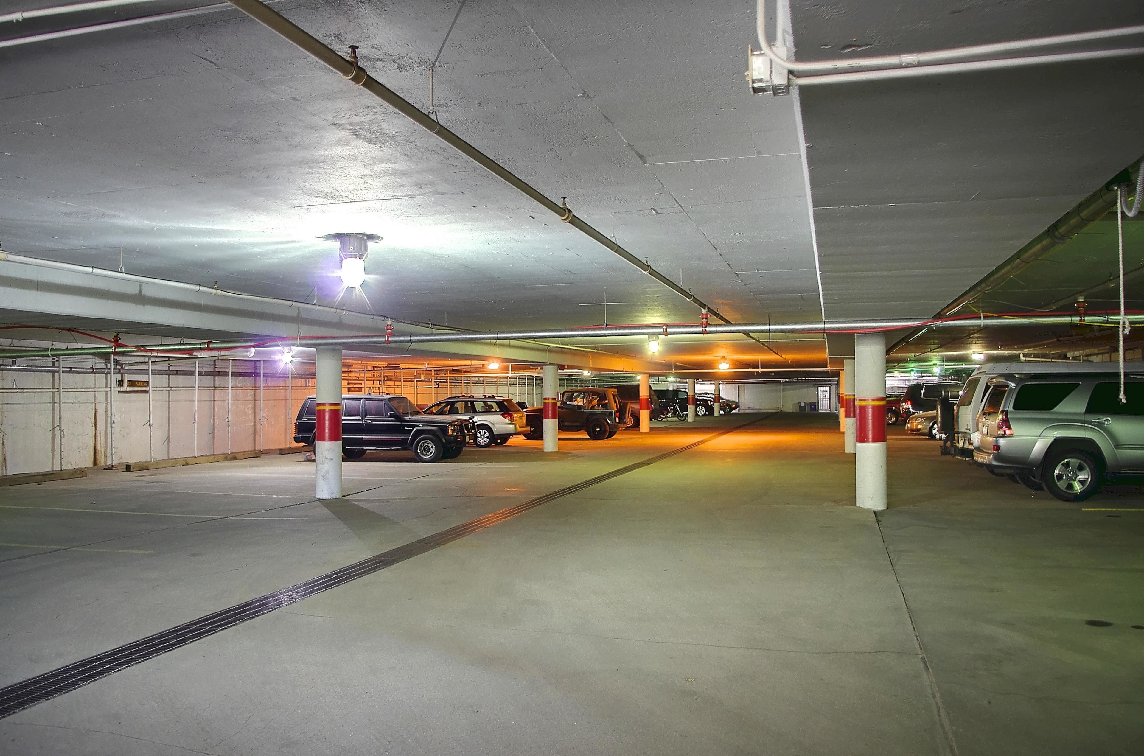 Eine mehrgeschossige Parkgarage mit Betonpfeilern, Überkopfrohren und einigen parkenden Fahrzeugen.