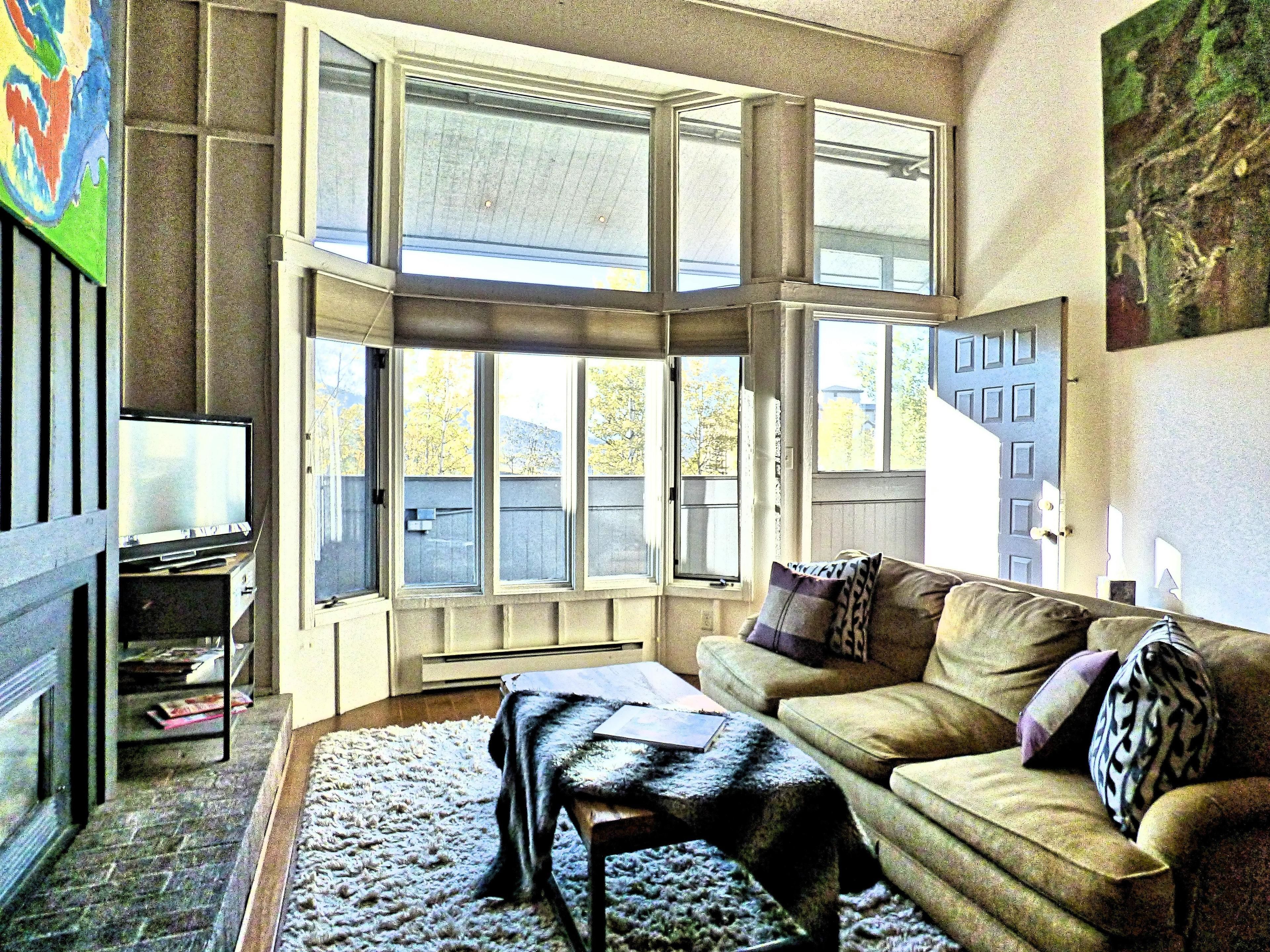 A living room with a large window, a sofa, a coffee table, and a television.