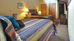 A bedroom with two beds, a ceiling fan, wooden doors, and a small table with lamps. - Lift Tickets Newly Remodeled Sleeps 8 Pool, Hot Tubs,fireplace, Private Deck (Steamboat Springs)