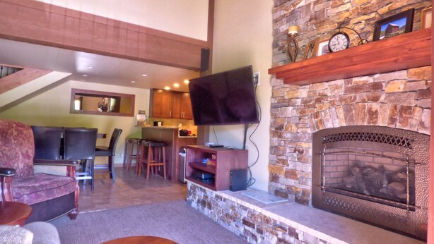 A spacious living area with a stone fireplace, wooden furniture, and a television mounted on the wall. - Lift Tickets Newly Remodeled Sleeps 8 Pool, Hot Tubs,fireplace, Private Deck (Steamboat Springs)
