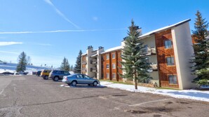 A multi-story residential building with a brick facade, balconies, and a parking area with several cars. - Lift Tickets Newly Remodeled Sleeps 8 Pool, Hot Tubs,fireplace, Private Deck (Steamboat Springs)
