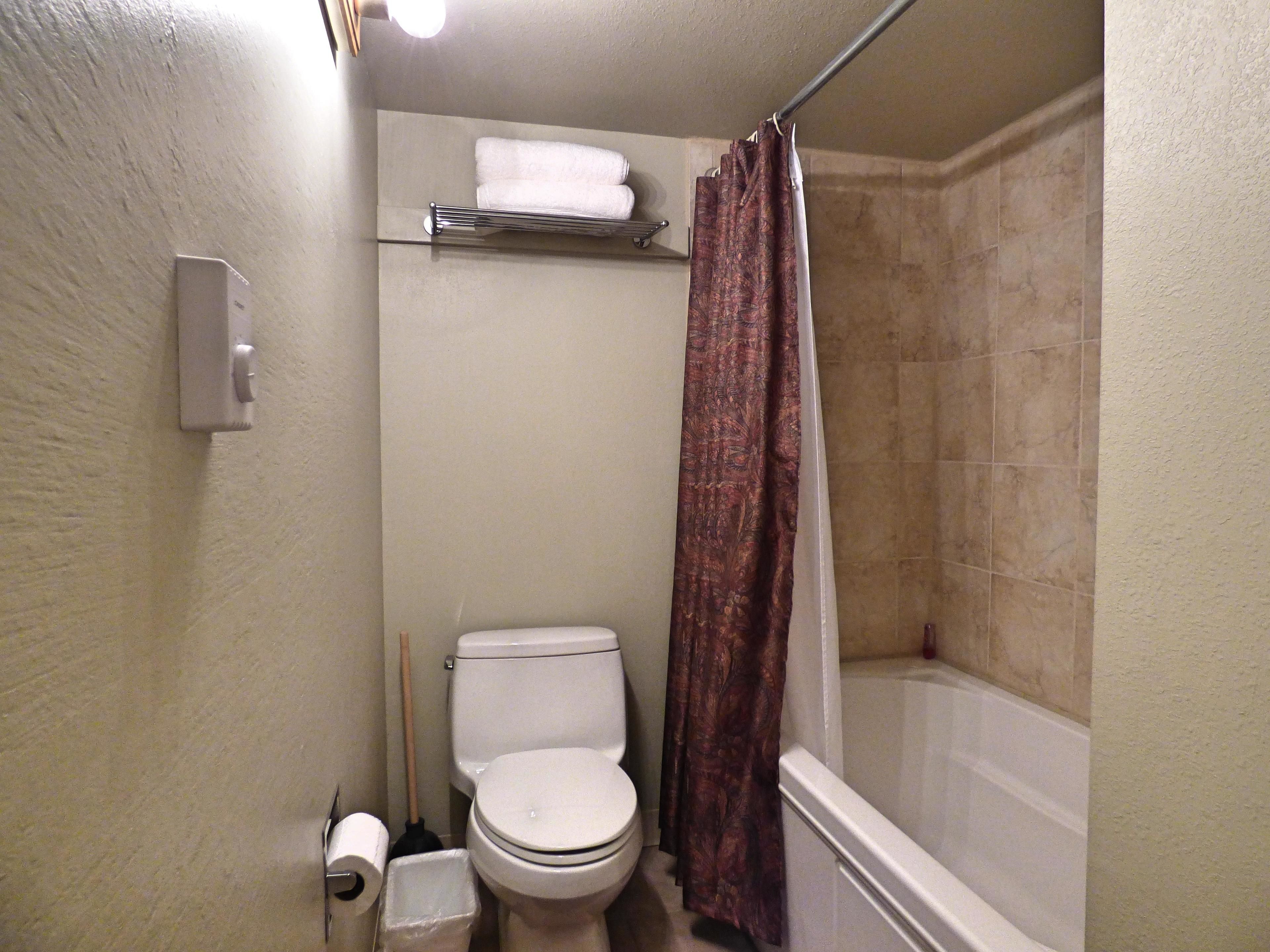 A small bathroom with a toilet, a shower curtain, a towel rack, and a toilet paper holder.