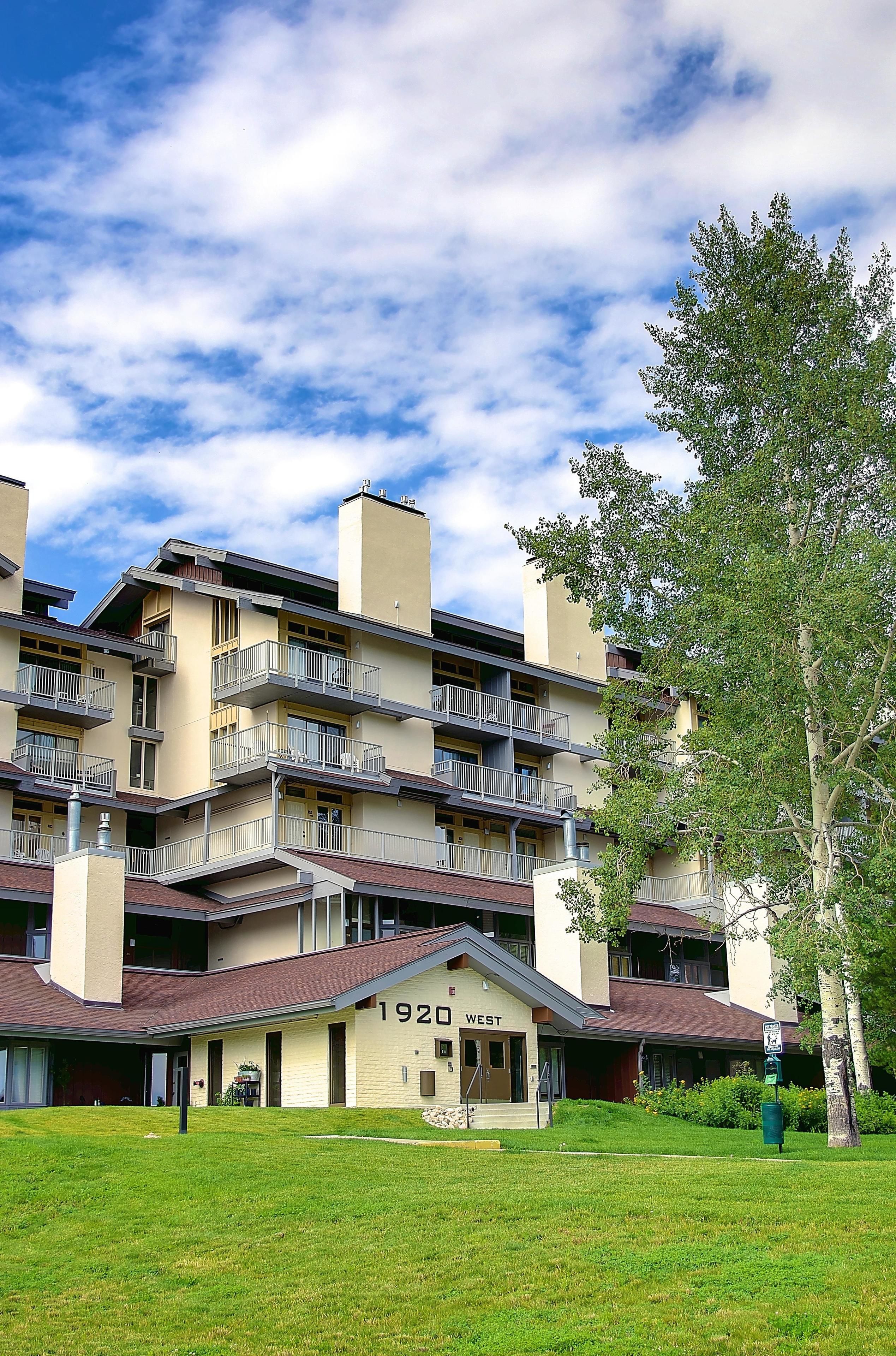 A multi-story building with balconies, a sign reading "1920 WEST," and a well-maintained lawn.