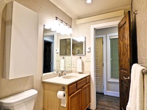 A bathroom with a toilet, sink, mirror, and wooden cabinets.