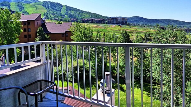 A balcony with a view of a green landscape, buildings, and mountains. - Private Deck Mountain Views Babbling Creek Sleeps 4 (Steamboat Springs)