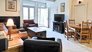A living room with a sofa, armchair, coffee table, TV stand, and dining area with chairs. - Lift Tickets Near Ski Hot Tubs Wifi Fireplace, Multi-level Unit (Steamboat Springs)