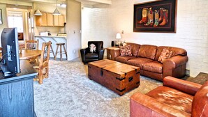 A living room with a leather couch, a wooden coffee table, and a vintage suitcase. There is a kitchen area with wooden cabinets and a dining table with chairs. - Lift Tickets Near Ski Hot Tubs Wifi Fireplace, Multi-level Unit (Steamboat Springs)