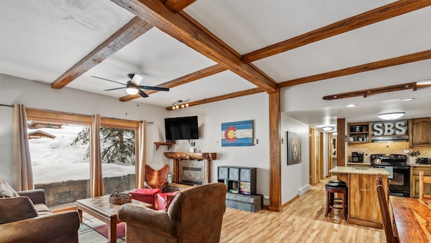 A spacious living room with a fireplace, wooden ceiling beams, and a large window overlooking a snowy landscape. - Lift Tickets Ground Floor Pool, Hot Tubs, Near Mtn, Fireplace Shuttle (Steamboat Springs)