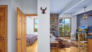 Een gezellige kamer met een stenen openhaard, houten meubels en een groot raam met uitzicht op de omgeving.