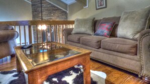 A living room with a brown sofa, a glass coffee table, and a stone accent wall. - Lift Tickets Shuttle & Hottub, Pool, Near Ski Mountain Area (Steamboat Springs)