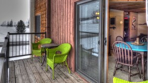 A wooden deck with green chairs and a table, a sliding glass door leading to an interior dining area, and a snowy landscape visible through the door. - Lift Tickets Shuttle & Hottub, Pool, Near Ski Mountain Area (Steamboat Springs)