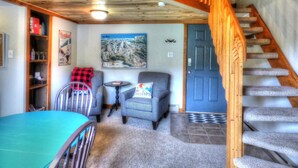 A cozy room with a wooden staircase, a blue door, two checkered chairs, a small table, and a bookshelf. - Lift Tickets Shuttle & Hottub, Pool, Near Ski Mountain Area (Steamboat Springs)