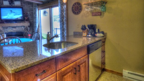 A kitchen with granite countertops, wooden cabinets, a built-in dishwasher, a coffee maker, and a clock on the wall. - Lift Tickets Shuttle & Hottub, Pool, Near Ski Mountain Area (Steamboat Springs)