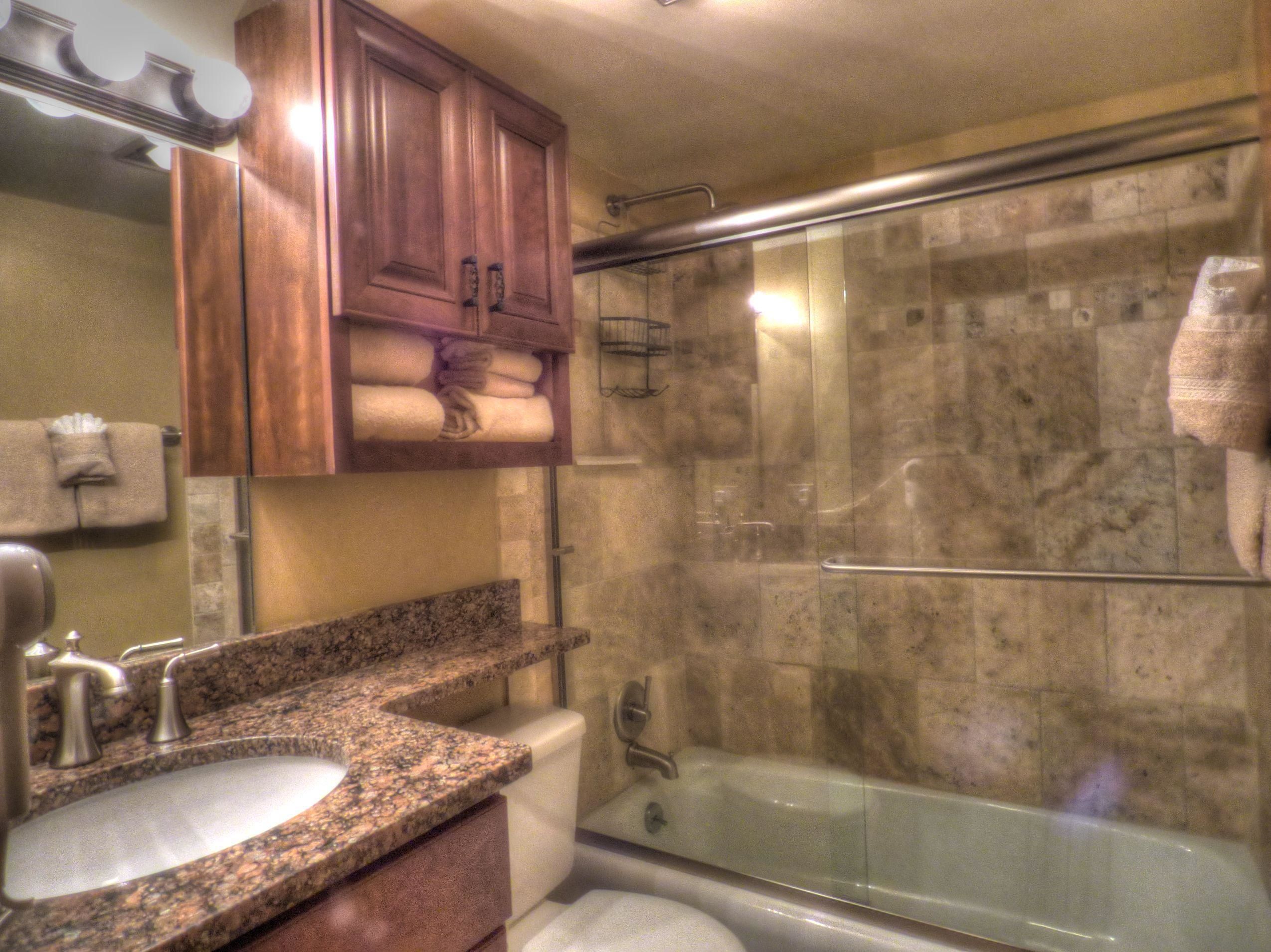 A bathroom with a granite countertop sink, a toilet, a glass-enclosed shower, and wooden cabinets above the sink.