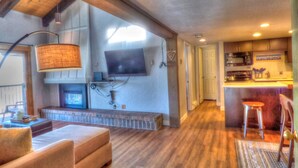 A modern living room with a fireplace, a television mounted on the wall, and a kitchen area with a bar. - Lift Tickets Pool, Hot Tubs, Shuttle & Private Deck Mountain Village (Steamboat Springs)