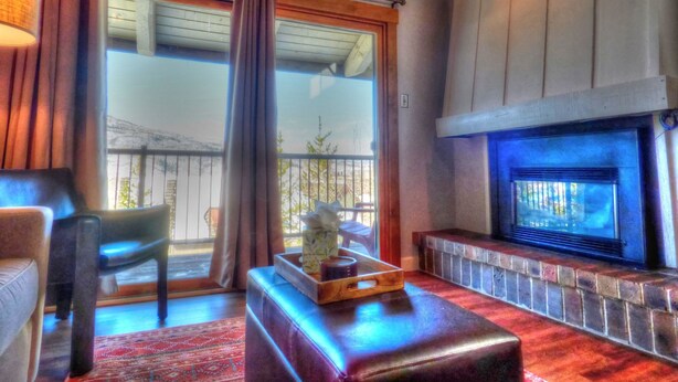 A cozy living room with a fireplace, a sofa, a coffee table, and a view of the outdoors through large windows. - Lift Tickets Pool, Hot Tubs, Shuttle & Private Deck Mountain Village (Steamboat Springs)