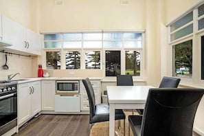 Una cocina con gabinetes blancos, microondas, estufa y un comedor con mesa y sillas.