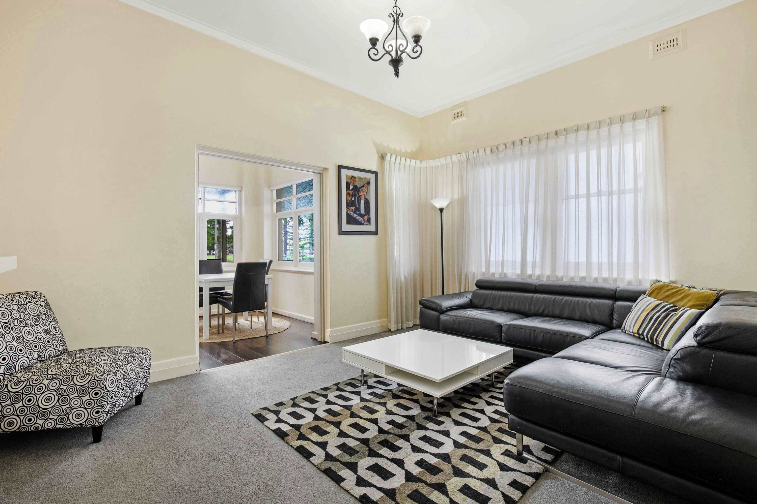 A living room with a sofa, a patterned armchair, a coffee table, a floor lamp, and a large window with curtains.