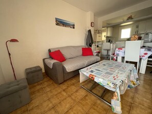 A cozy living room with a sofa, a dining table, and a kitchen area in the background.