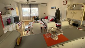 Ett kompakt bostadsutrymme med en matplats, ett litet kök och utsikt genom fönstret.