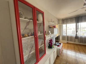 A room with a large window, a red-framed cabinet with glass doors, and a small table with a vase of flowers.