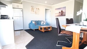 Un espacio habitable compacto con kitchenette, un sofá azul, una mesa de centro de madera, una mesa de comedor con sillas y obras de arte en las paredes.