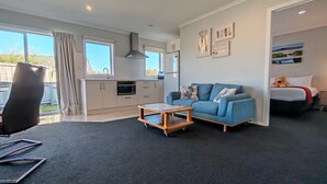 Una sala de estar moderna con un sofá azul, una mesa de centro de madera y una zona de cocina con refrigerador y estufa.
