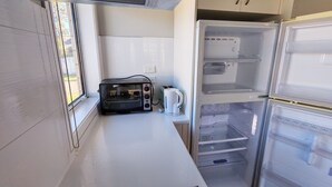 Una kitchenette compacta con tostadora, hervidor y un refrigerador pequeño.