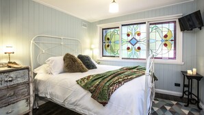 Ein Schlafzimmer mit Bett, Schminktisch, einem Fenster mit Buntglas und einem an der Wand befestigten Fernseher.