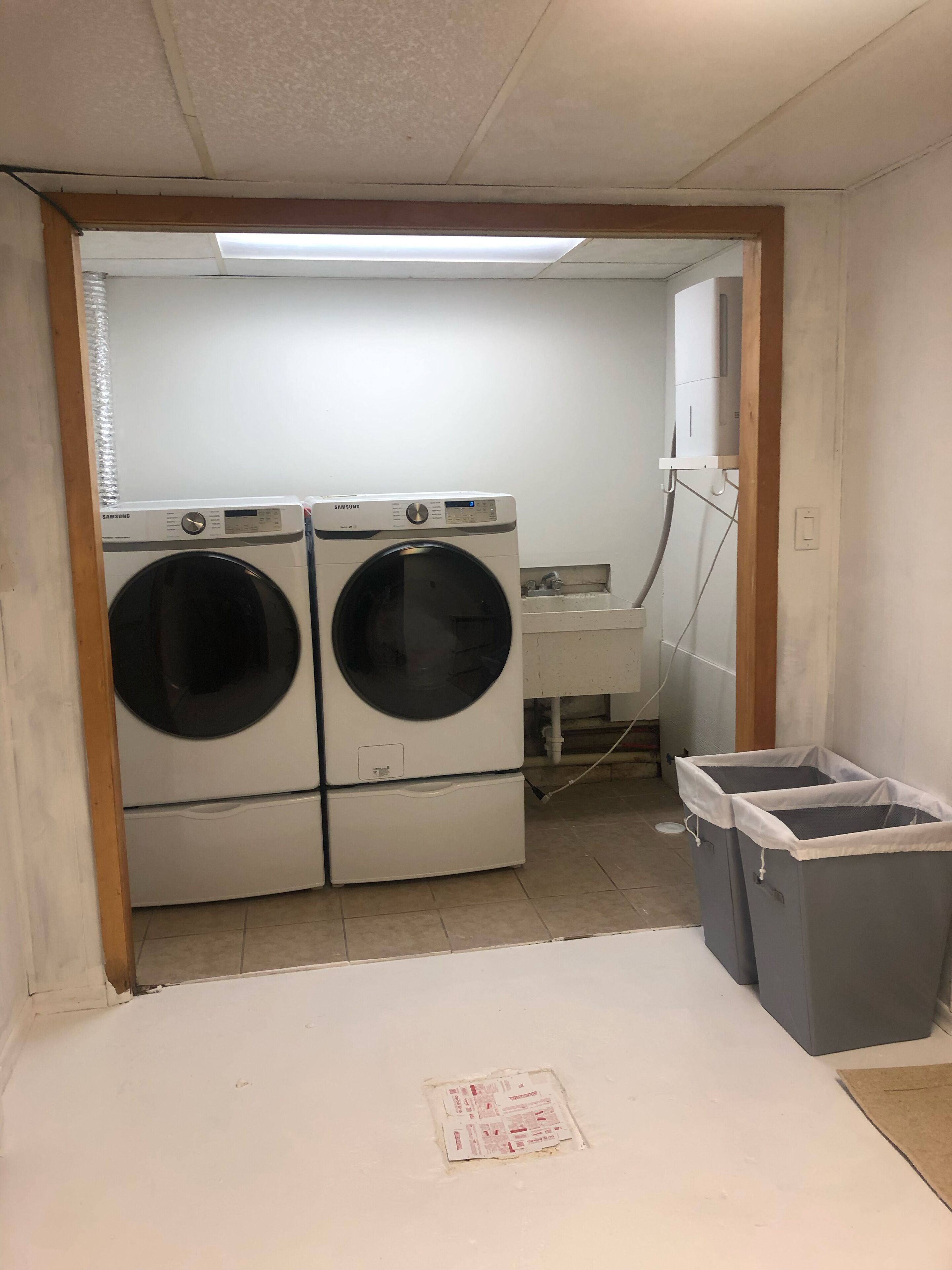 A laundry room with two Samsung washing machines, a sink, and two grey trash bins.