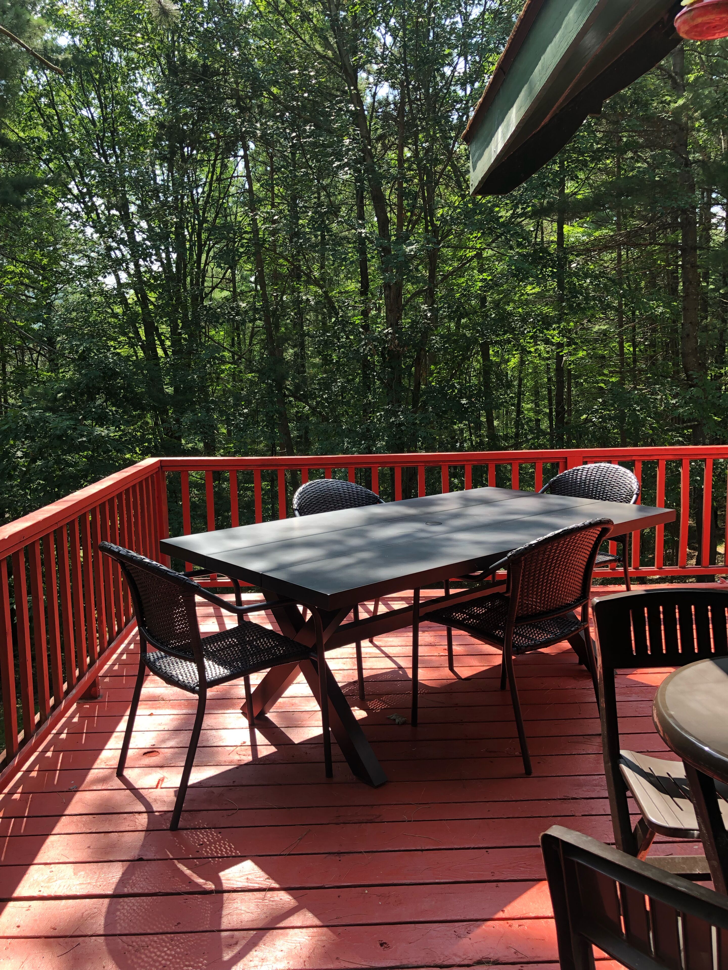 A wooden deck with a red railing, a table, and four chairs.