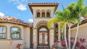 A Mediterranean-style house with a tiled roof, a central arched entrance, and a well-maintained garden with palm trees and shrubs. - Backyard Oasis, Luxurious, Magnificent-Villa Triton's Tide- Cape Coral- Roelens Vacations (Cape Coral)