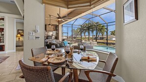 A dining area with a glass table and wicker chairs, overlooking a swimming pool and outdoor scenery. - Backyard Oasis, Luxurious, Magnificent-Villa Triton's Tide- Cape Coral- Roelens Vacations (Cape Coral)
