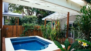 A rectangular hot tub with a white edge, surrounded by a wooden fence and lush greenery.