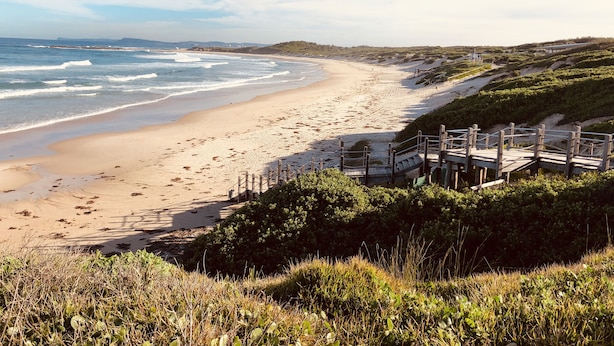 A beach with a wooden boardwalk leading to a sandy shore.
