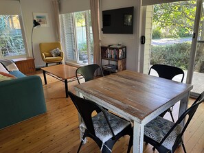 A room with a wooden dining table, chairs, a sofa, a bookshelf, and a TV.