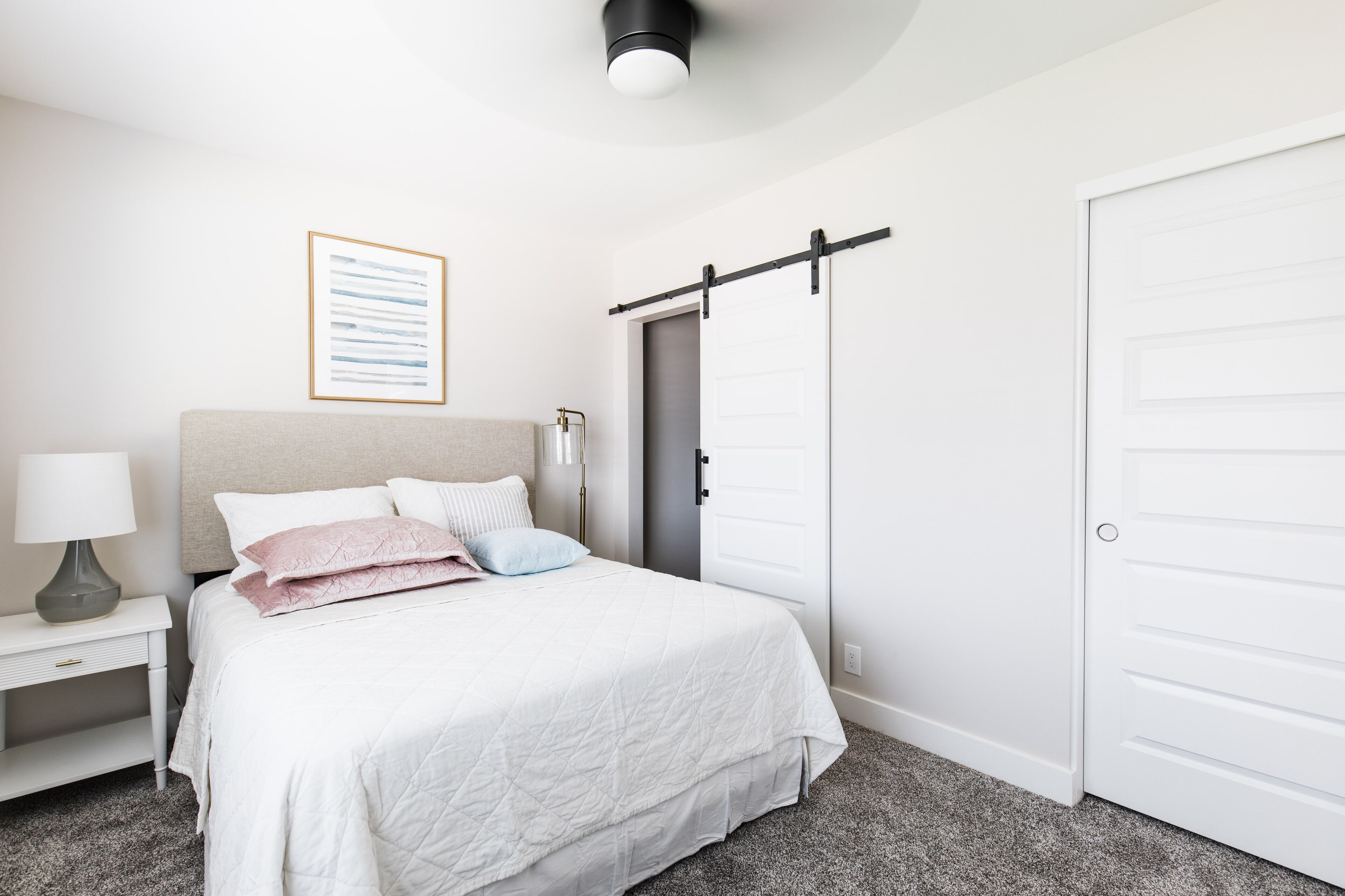 Un dormitorio con cama, mesita de noche, lámpara, un cuadro enmarcado, una puerta corrediza y un armario blanco.