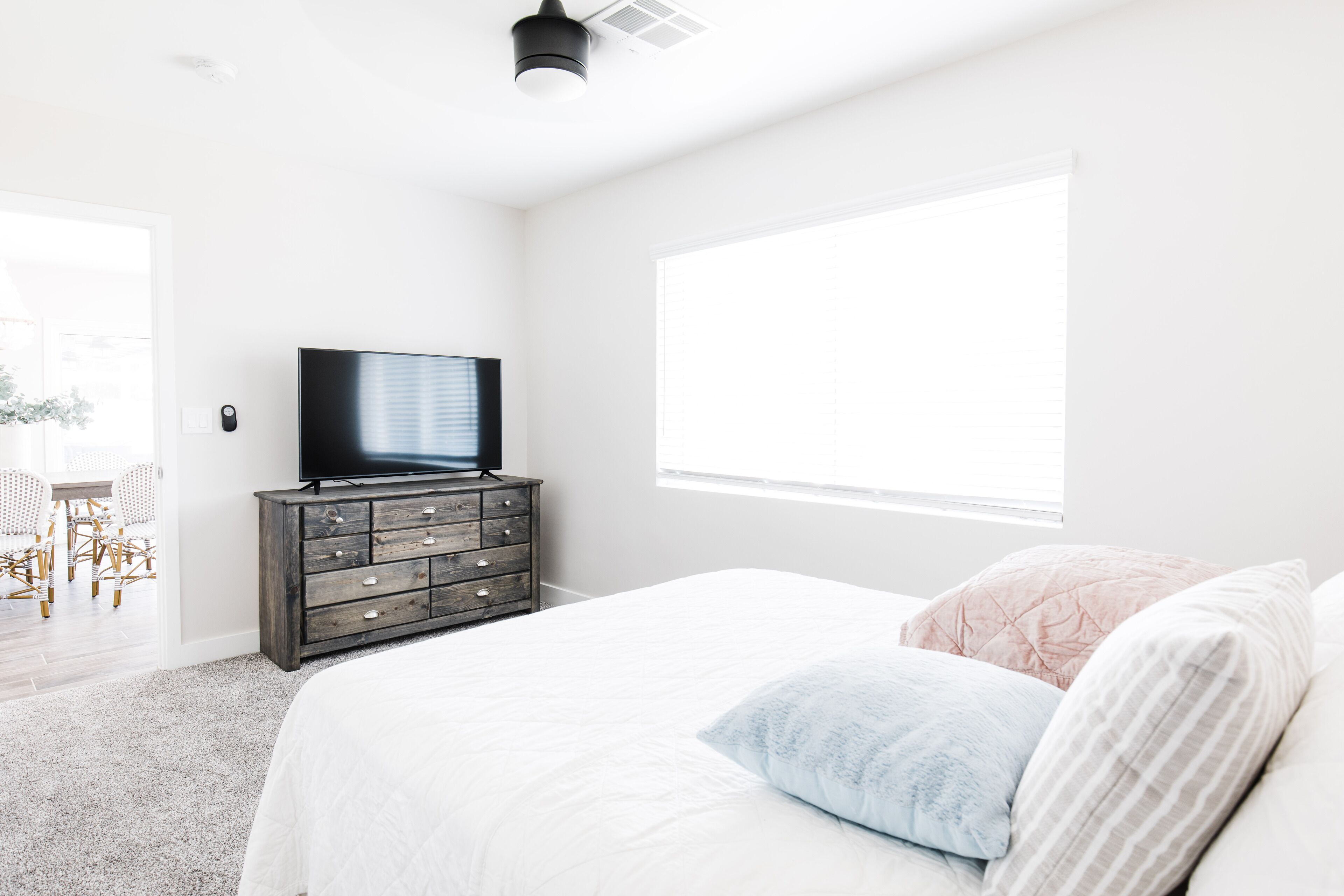 Un dormitorio con cama, cómoda, televisor y un ventanal amplio.