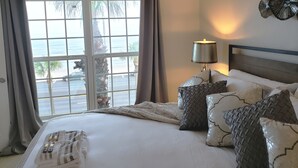 Ein Hotelzimmer mit einem großen Bett, einem Nachttisch, einer Lampe und Meerblick durch ein Fenster.