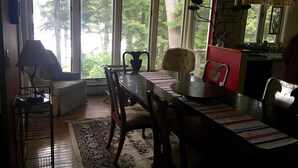 Un coin repas comprenant une table, des chaises, un tapis et une fenêtre donnant sur des arbres.