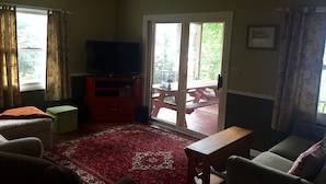 Un salon avec un téléviseur, un tapis rouge à motifs, une table en bois et un fauteuil vert.