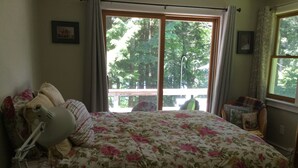 Une chambre avec un grand lit, une table de chevet avec une lampe, une fenêtre avec des rideaux et une vue sur les arbres à l’extérieur.