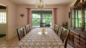 A dining room with a large table, chairs, a chandelier, a window with curtains, and a wooden cabinet. - New Braunfels Gruene River Front Property (New Braunfels)
