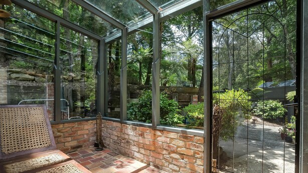 Ein Wintergarten mit einer Bank, Ziegelwänden und einer Glastür, die in einen Garten führt.