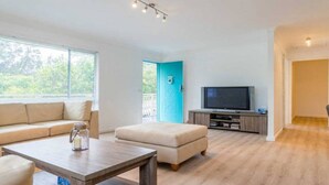 Un salon moderne comprenant un canapé, un pouf, une table basse et un téléviseur posé sur un meuble en bois.