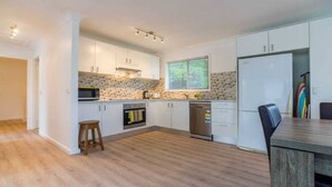 Une cuisine moderne avec des armoires blanches, un four à micro-ondes, un four et un lave-vaisselle. On y trouve un tabouret en bois et une table à manger avec des chaises.