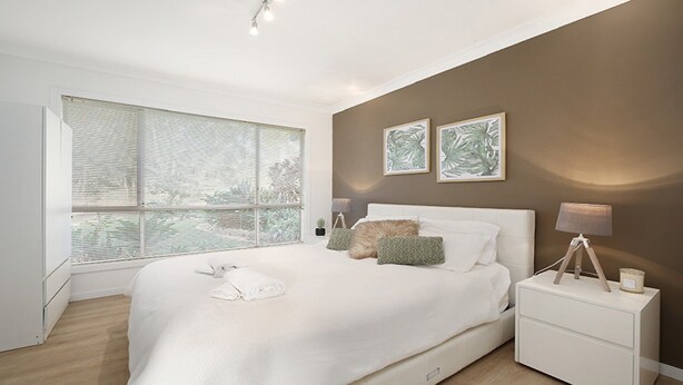 Une chambre moderne avec un grand lit, une table de chevet avec une lampe et deux tableaux encadrés au mur.