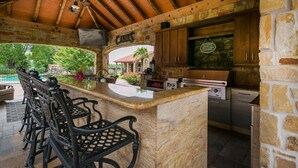 A stone kitchen with a bar area, wooden ceiling beams, and a stone wall with a sign.